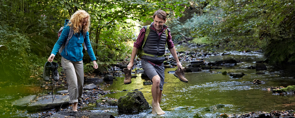 Over 50s couple paddling through a stream in a forest and enjoying one of the most romantic first date ideas.