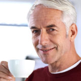 grey haired man inside drinking tea