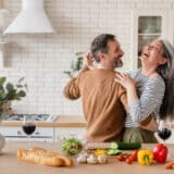 Mature couple dancing in front of a pile of vegetables in the kitchen.